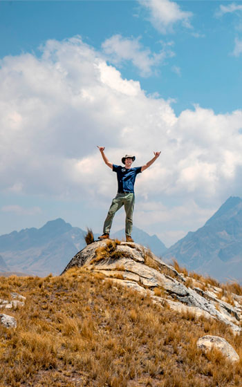 Turistas celebrando y levantando las manos con el impresionante paisaje montañoso andino de fondo. Ruta de la Cantera Inca en Perú.