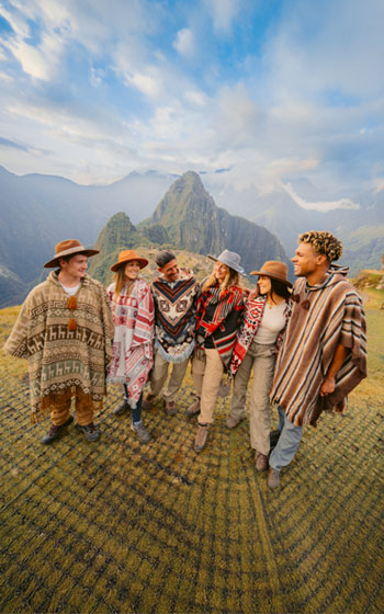 Grupo de turistas posando con ponchos andinos tradicionales en el área de la ciudadela Inca de Machu Picchu.