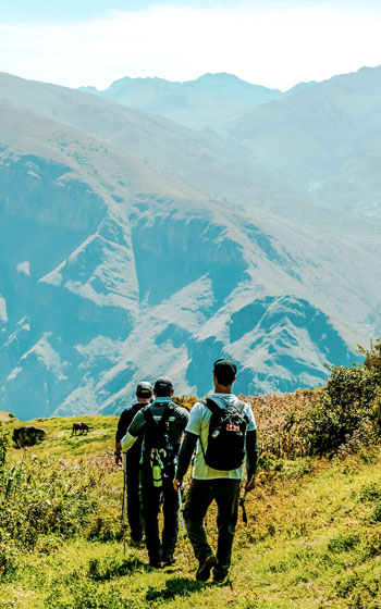 Turistas caminando por el sendero escénico hacia el sitio arqueológico de Huchuy Qosqo, rodeados del impresionante paisaje andino y la historia Inca de Perú.