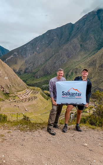 Turistas disfrutando de una vista panorámica del sitio arqueológico de Llactapata, rodeado de exuberantes montañas andinas y antiguas ruinas incas en Perú.