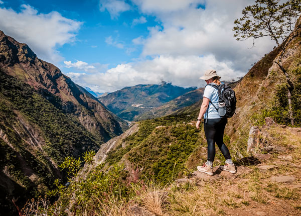 Turista disfrutando de una vista panorámica del exuberante paisaje andino a lo largo del Inca Jungle Trail, contemplando el vibrante escenario de montañas y bosques tropicales.