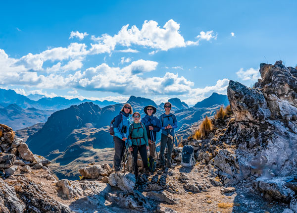 Turistas de pie en la caminata Lares con las majestuosas montañas andinas elevándose detrás de ellos, capturando la belleza y la tranquilidad de esta ruta de trekking de gran altitud en Perú.
