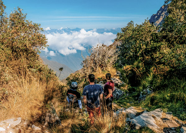 Turistas y su guía admirando las impresionantes vistas montañosas a lo largo del Camino Inca, rodeados por el majestuoso paisaje y la rica historia de los Andes peruanos.