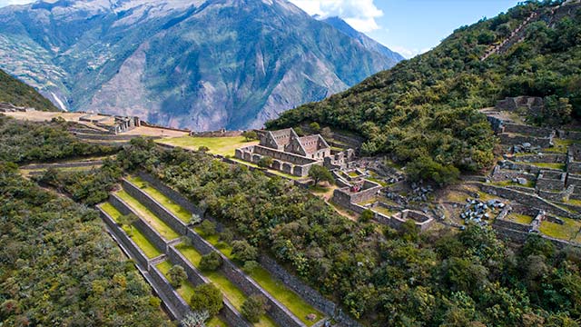 Vista panorámica de Choquequirao, mostrando sus antiguas calles, escaleras y terrazas aún cubiertas por abundante vegetación, resaltando la impresionante arquitectura inca y los paisajes andinos que la rodean.