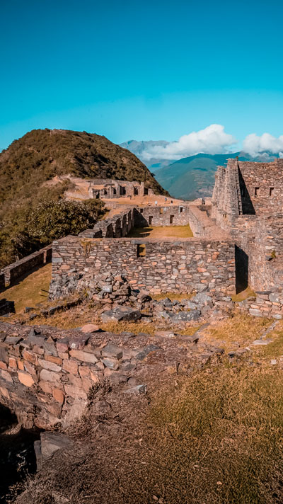 Magníficas construcciones de las ruinas de Choquequirao situadas en medio de imponentes montañas andinas, mostrando la arquitectura inca y la majestuosidad del paisaje peruano.