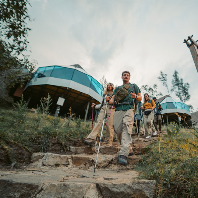 Un grupo de excursionistas con mochilas llegando al lujoso campamento Mountain Sky View, que cuenta con modernos domos de cristal y una vista impresionante de las montañas andinas de fondo.