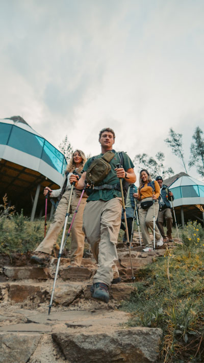 Un grupo de excursionistas con mochilas llegando al lujoso campamento Mountain Sky View, que cuenta con modernos domos de cristal y una vista impresionante de las montañas andinas de fondo.