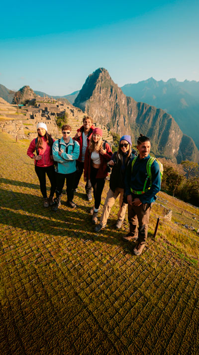 Grupo de turistas posando para una foto con las majestuosas ruinas de Machu Picchu de fondo, disfrutando de la belleza histórica y natural de los Andes peruanos.