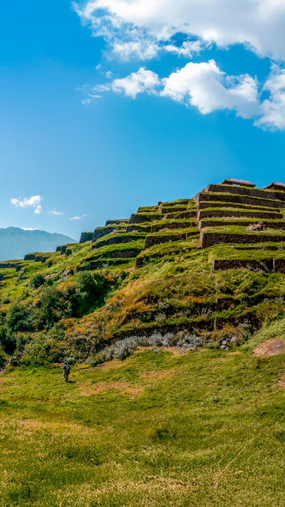 Impresionante vista del Sitio Arqueológico Pre-Inca de Huchuy Qosqo y sus terrazas, ubicado en medio de majestuosas montañas andinas, destacando la arquitectura ancestral y los paisajes peruanos.