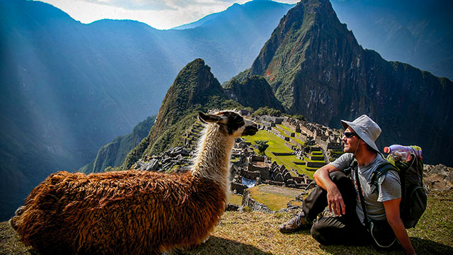 Preciosa foto del encuentro de los habitantes naturales de Machu Picchu con un visitante, una llama y su huésped en el Santuario Inca.