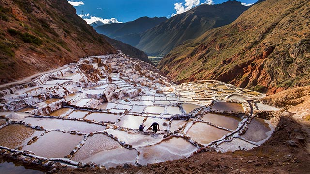 Pareja de turistas con ponchos andinos en las Salineras de Maras, enclavadas en las montañas de los Andes sobre el Valle Sagrado de los Incas, admirando sus antiguas pozas de sal.
