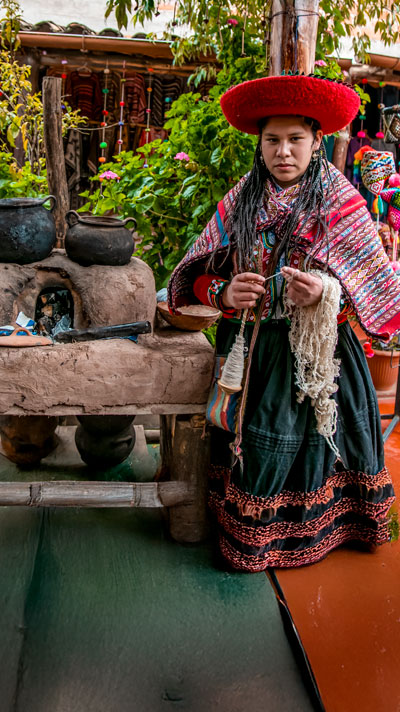 Mujer andina vestida con su traje típico, confeccionando tejidos tradicionales a mano y preservando las antiguas técnicas artesanales de los Andes peruanos.