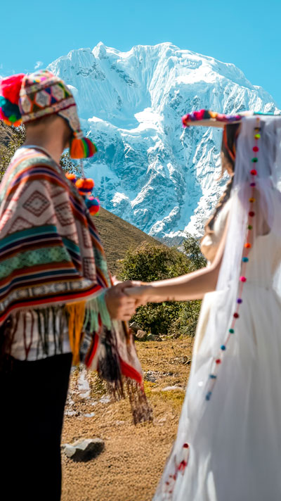 Pareja de turistas participando en una ceremonia de boda andina en Soraypampa, rodeada de las majestuosas montañas sagradas de Salkantay y Humantay, disfrutando de una experiencia cultural única en los Andes peruanos.