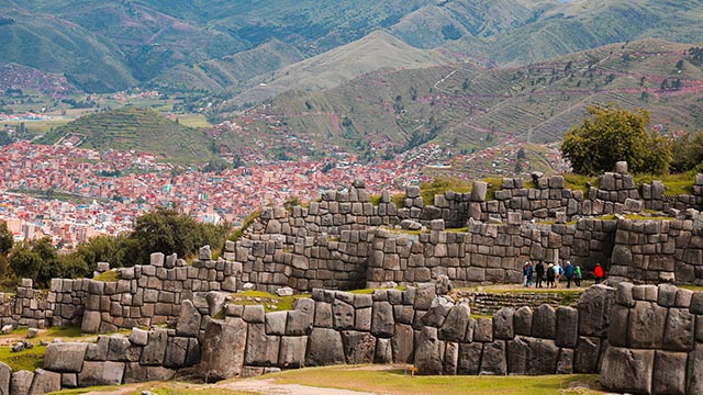 Vista panorámica del complejo arqueológico inca de Sacsayhuamán con turistas explorando sus imponentes muros de piedra y el paisaje andino.