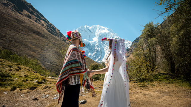 Pareja de turistas participando en una ceremonia de boda andina en Soraypampa, rodeada de las majestuosas montañas sagradas de Salkantay y Humantay, disfrutando de una experiencia cultural única en los Andes peruanos.