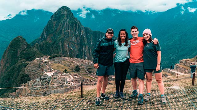 Grupo de turistas posando para una foto con las majestuosas ruinas de Machu Picchu de fondo, disfrutando de la belleza histórica y natural de los Andes peruanos.