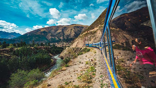 Grupo de turistas disfrutando de increíbles vistas de los Andes durante su viaje en tren hacia Machu Picchu, rodeados de majestuosos paisajes peruanos.