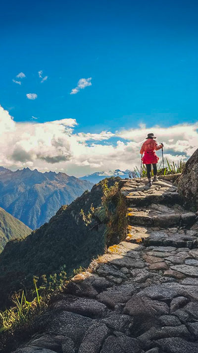 Turista caminando por el increíble Camino Inca antiguo hacia Machu Picchu, cerca del acantilado y rodeado de impresionantes paisajes andinos.