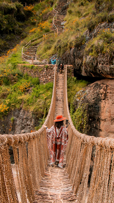 Turista visitando el puente Queswachaka, el último puente inca aún tejido con fibras de ichu, rodeado de un impresionante paisaje andino.