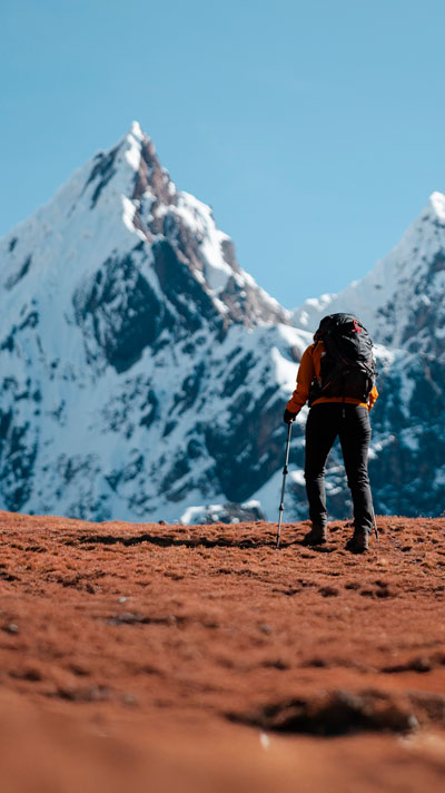 Turista con ropa de trekking caminando en dirección a la montaña sagrada de Ausangate, rodeado de majestuosos paisajes altoandinos en Perú.