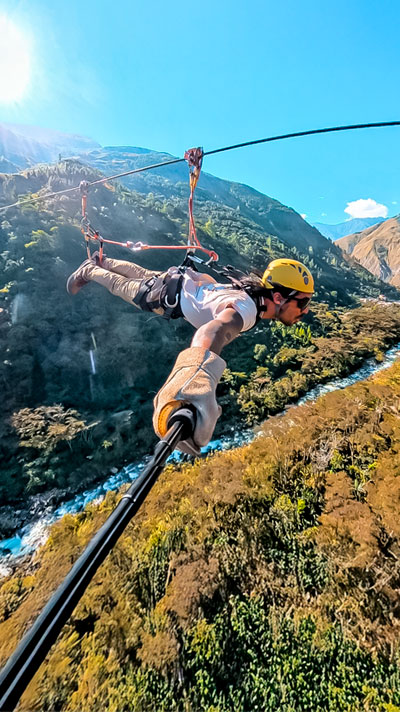 Turista disfrutando de la tirolesa en la ruta Inca Jungle hacia Machu Picchu, rodeado de exuberantes paisajes andinos y bosques tropicales del Perú.