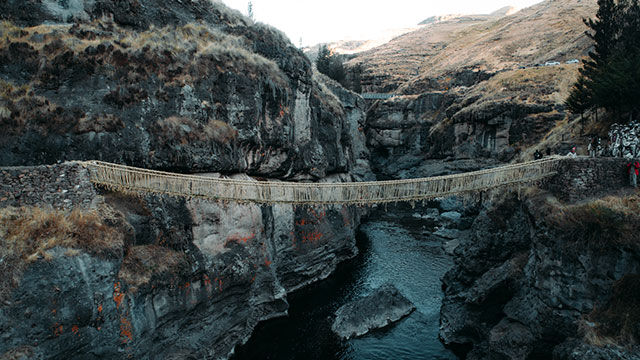 Turista visitando el puente Queswachaka, el último puente inca aún tejido con fibras de ichu, rodeado de un impresionante paisaje andino.