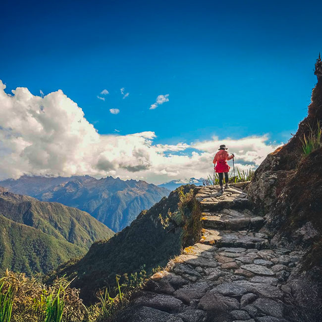 Turista caminando por el increíble Camino Inca antiguo hacia Machu Picchu, cerca del acantilado y rodeado de impresionantes paisajes andinos.