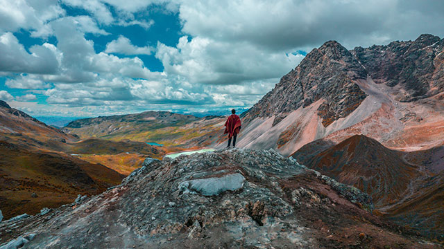 Turista con ropa de trekking caminando en dirección a la montaña sagrada de Ausangate, rodeado de majestuosos paisajes altoandinos en Perú.