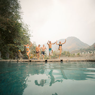 Grupo de turistas disfrutando de las piscinas de aguas termales cristalinas de Cocalmayo en Santa Teresa, rodeados de vegetación tropical.
