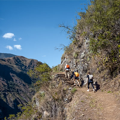 Grupo de jóvenes aventureros con equipo de trekking recorriendo un sendero estrecho en las montañas de la selva alta durante el Inca Jungle Trek.
