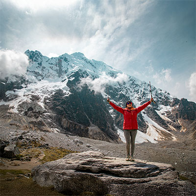 Turista celebrando con bastones en la cima del Abra Salkantay a 4,630 msnm con el majestuoso nevado Salkantay detrás.