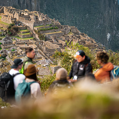 Un grupo alegre de excursionistas y su guía de montaña profesional posando con los brazos en alto frente a la ciudadela de Machu Picchu, celebrando el final del trekking.