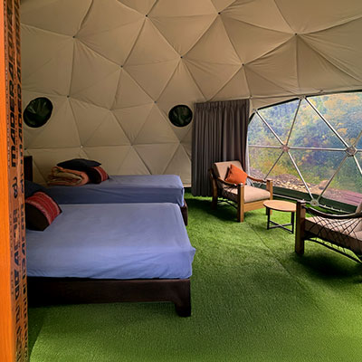 Vista interior de un acogedor domo geodésico en el campamento Salkantay Mountain Domes en Soraypampa, mostrando camas confortables y un panel transparente con vista al accidentado paisaje andino.