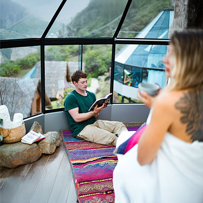 Pareja de turistas relajándose dentro de un domo de cristal de lujo en Mountain Sky View, Collpapampa, durante el Salkantay Trek.