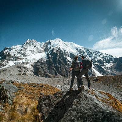 Pareja de turistas contemplando la cumbre nevada de la montaña Salkantay desde el sendero de trekking en los Andes de Cusco, Perú.