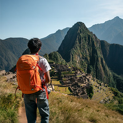 Turista con mochila de montaña contemplando la ciudadela inca de Machu Picchu desde el mirador superior tras completar su ruta de senderismo.