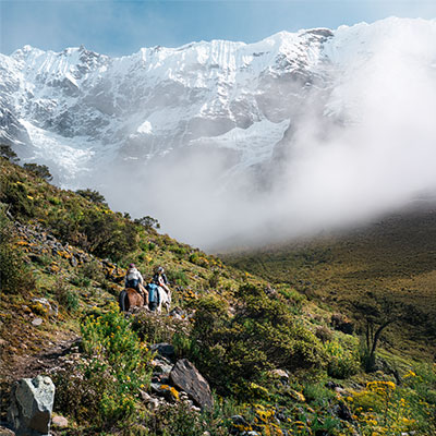 Turistas cabalgando por el sendero hacia la Laguna Humantay con vistas impresionantes al glaciar y montañas de Cusco.