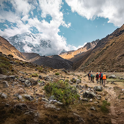 Grupo de turistas realizando una caminata por el sendero del Salkantay Trek con vistas panorámicas al glaciar y montañas nevadas en Cusco.