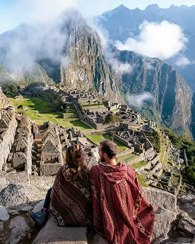 Pareja de turistas vestidos con ponchos andinos frente a Machu Picchu
